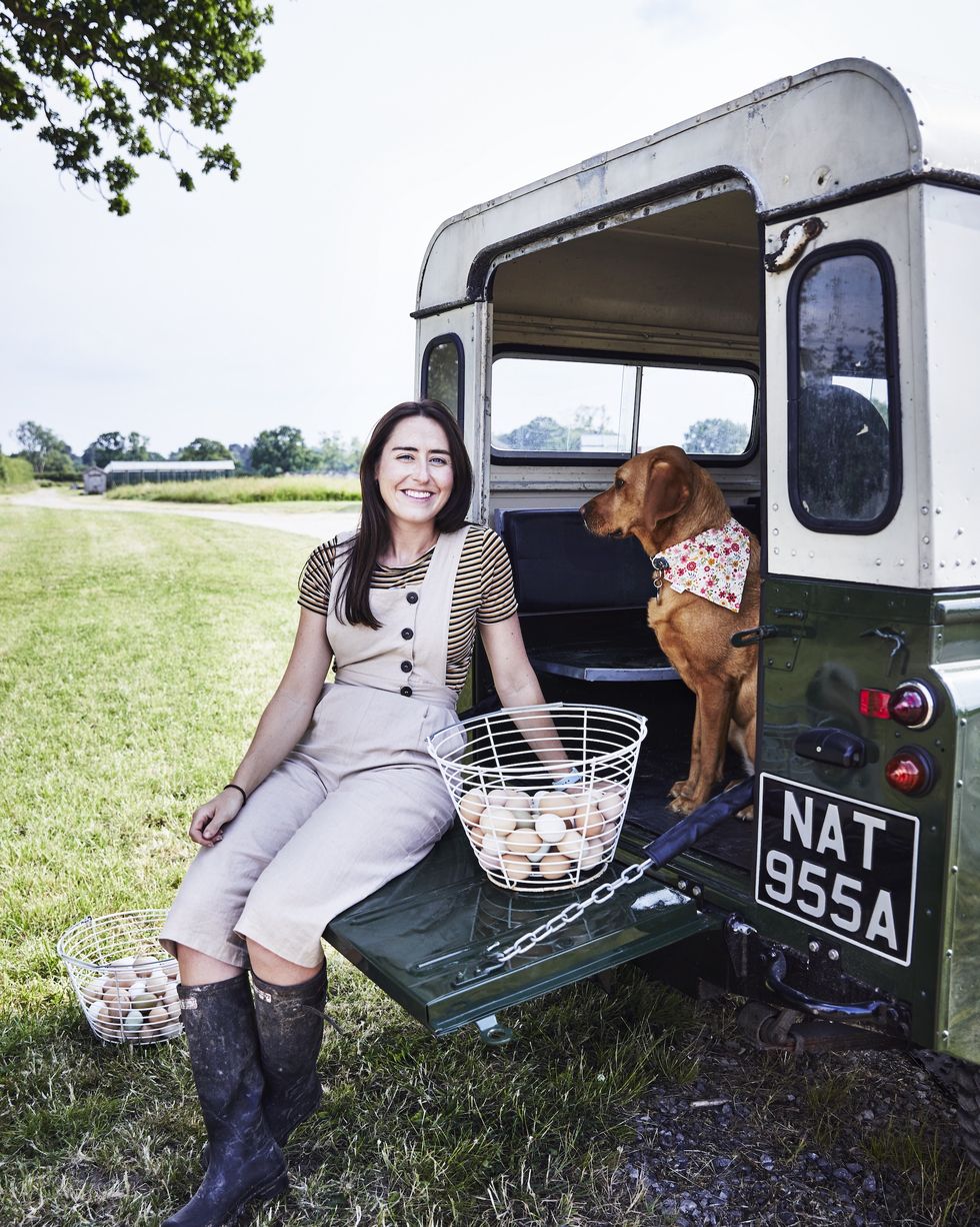 amelia strong wearing wellies leaning on the open boot of her landrover with her labrador and baskets of eggs