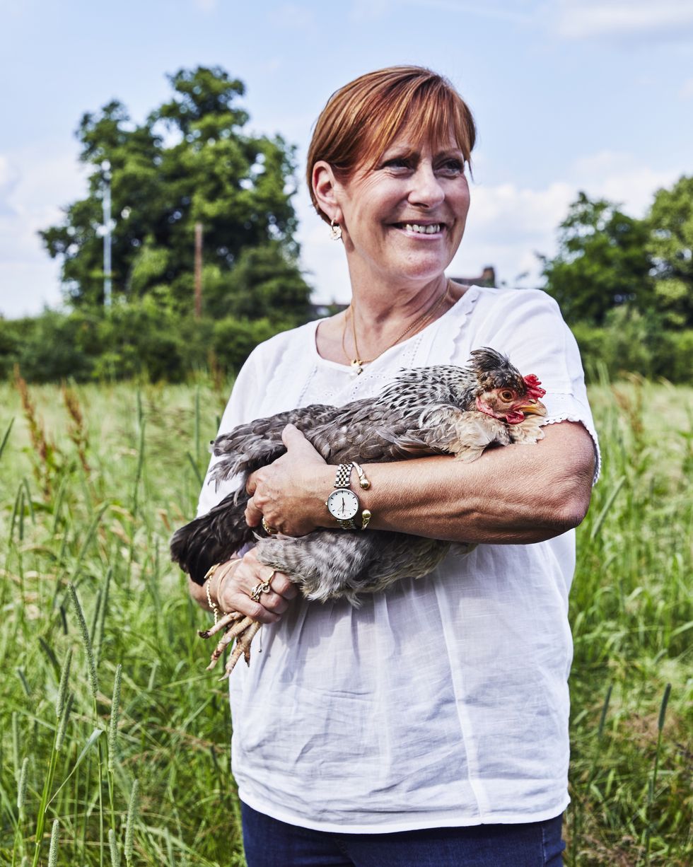 a woman with short red hair standing in a field holding a rare breed hen