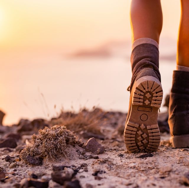 close up of unrecognizable hiker in hiking boots walking on a hill above the sea at sunset copy space