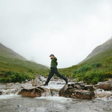 Hiker crossing river in Mountain Valley, Glencoe, Scotland hiker crossing river in mountain valley, glencoe, scotland