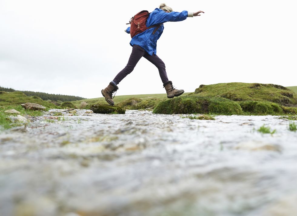 hiker stepping across stream in countryside