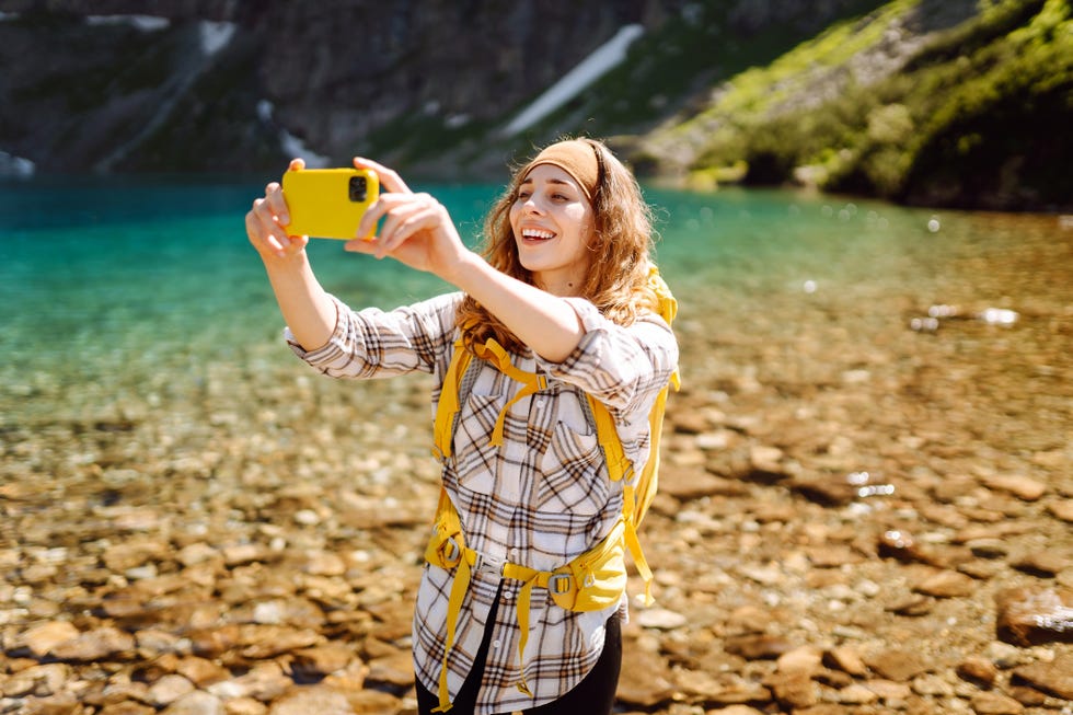 young woman with mountains and lake in background taking selfie