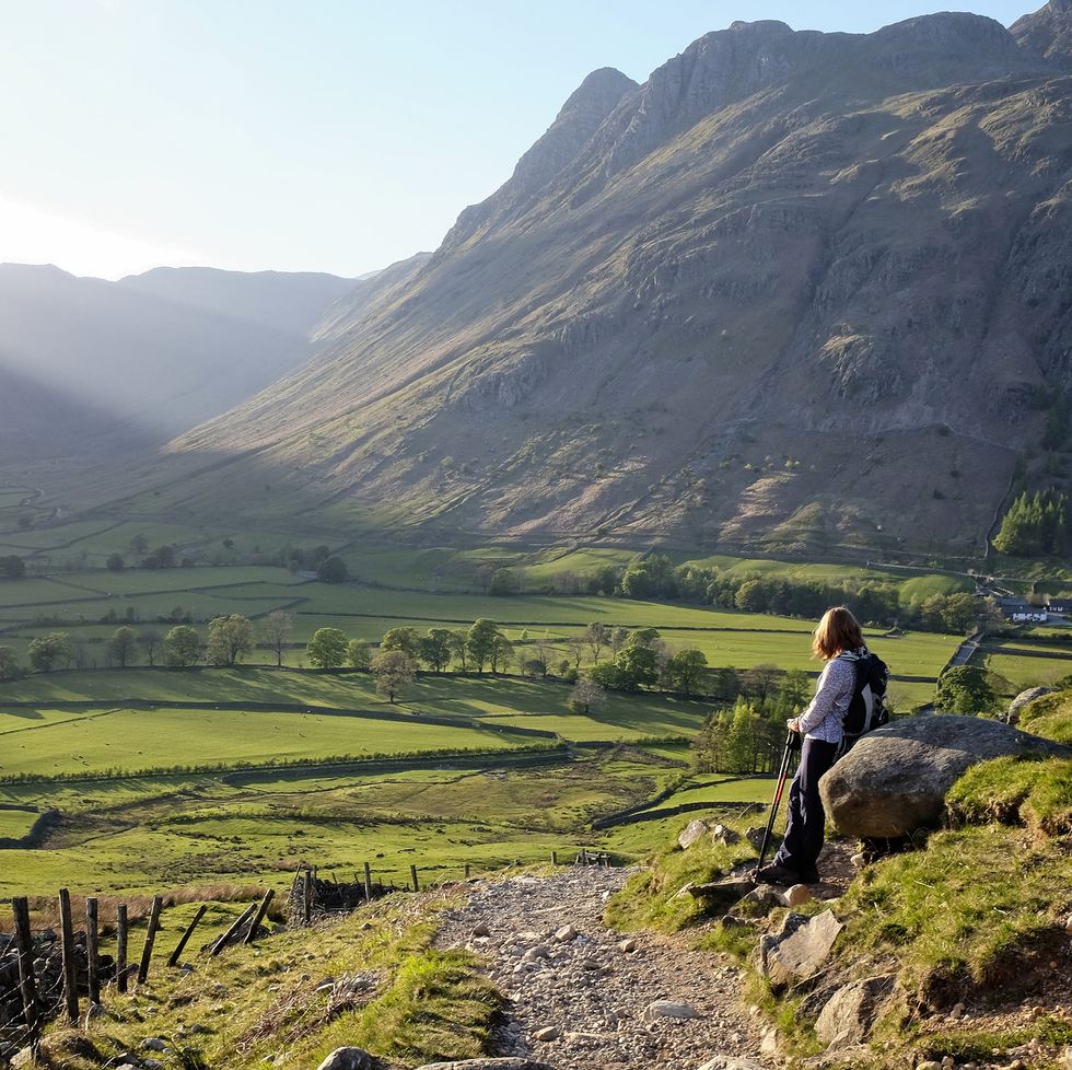 golden evening light spreads over the valley in great langdale with a hillwalker in the foreground