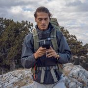 man with hiking backpack using phone on rocky trail