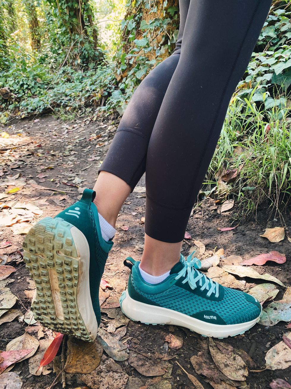 a model wears a pair of hilma sneakers and black leggings while walking on a trail to illustrate a hilma running shoes review 2023