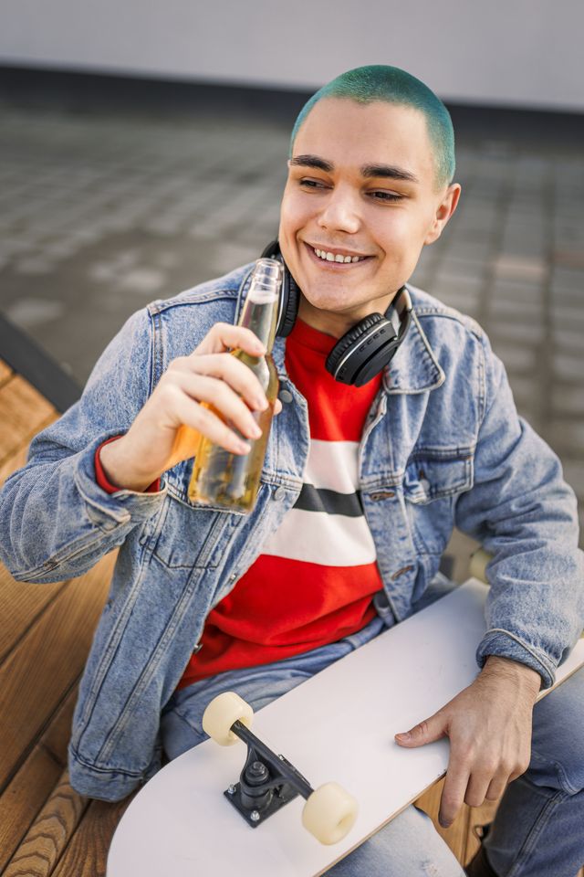 hipster male teenager listening music and drinking beer outdoors
