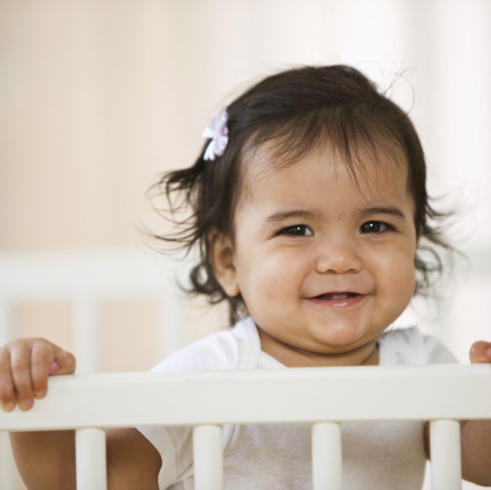 hispanic baby girl standing in crib