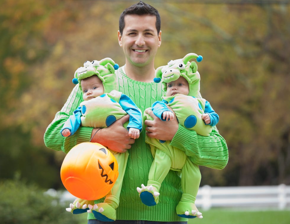 Hispanic father holding twin babies in Halloween costumes