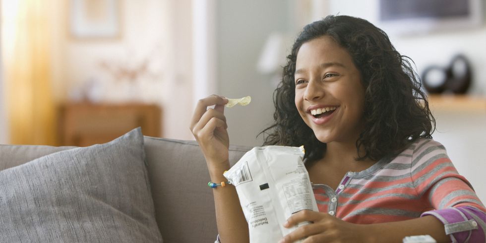 hispanic girl eating potato chips on sofa