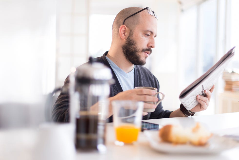 Hispanic man reading newspaper at breakfast