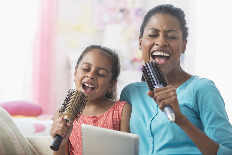 hispanic mother and daughter singing with hairbrushes and digital tablet