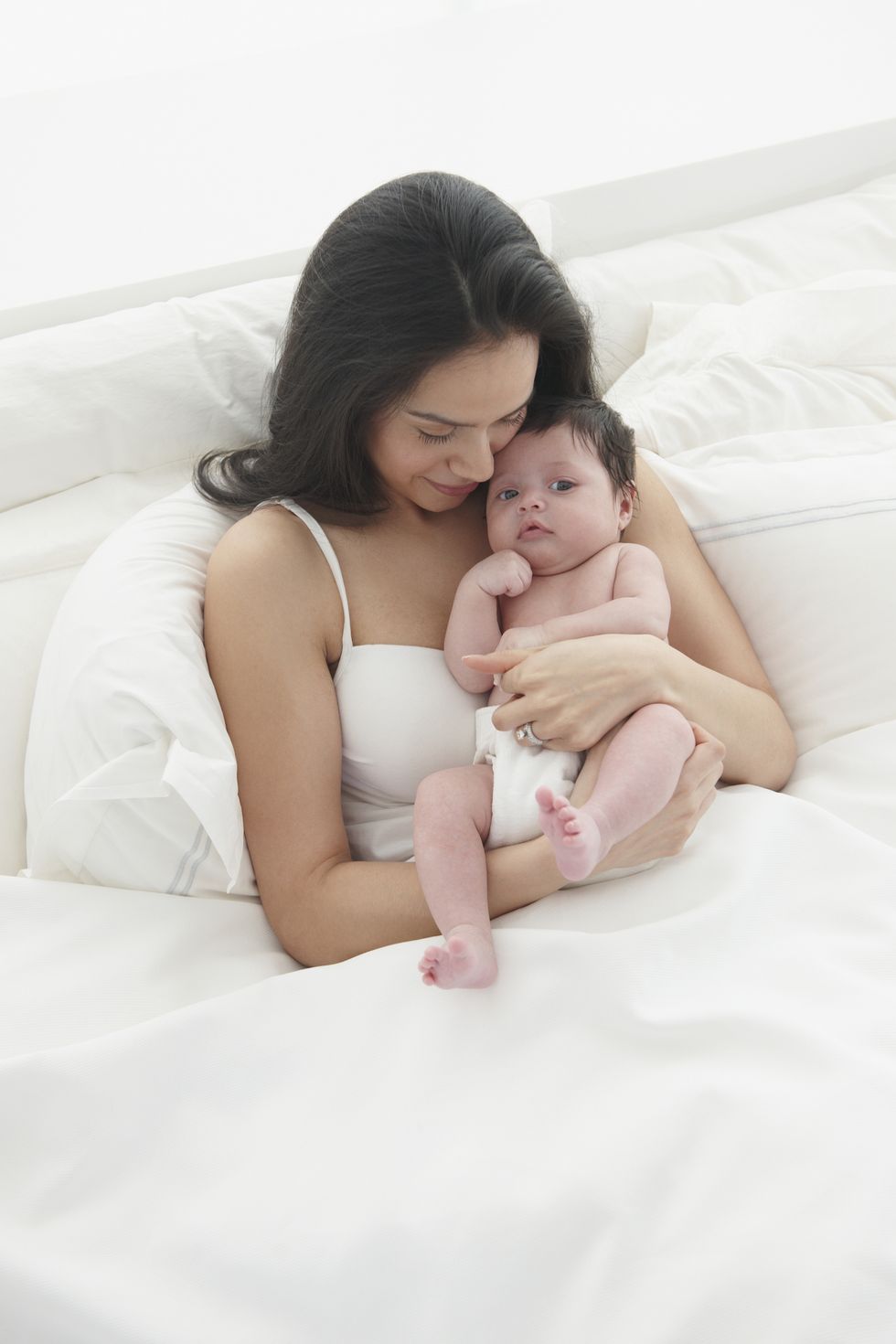 una madre incorpora a su bebeé cogiéndole en la cama para intentar aliviarle el hipo, que es uno de los ruidos raros que hacen los bebés