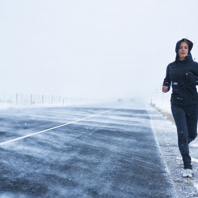 Hispanic woman jogging on snow covered road