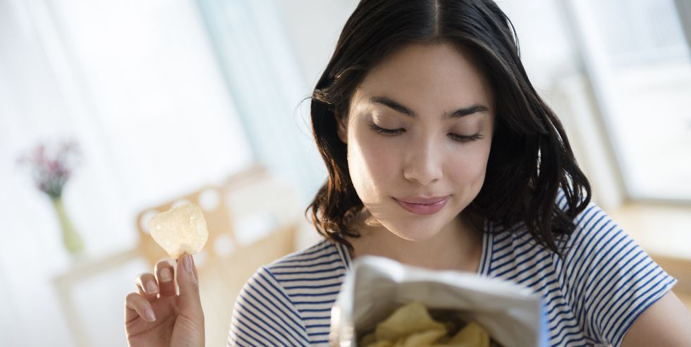 hispanic woman reading ingredients on bag of potato chips