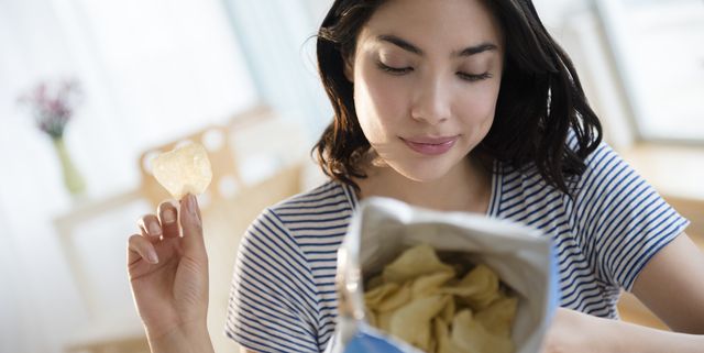 Hispanic woman reading ingredients on bag of potato chips