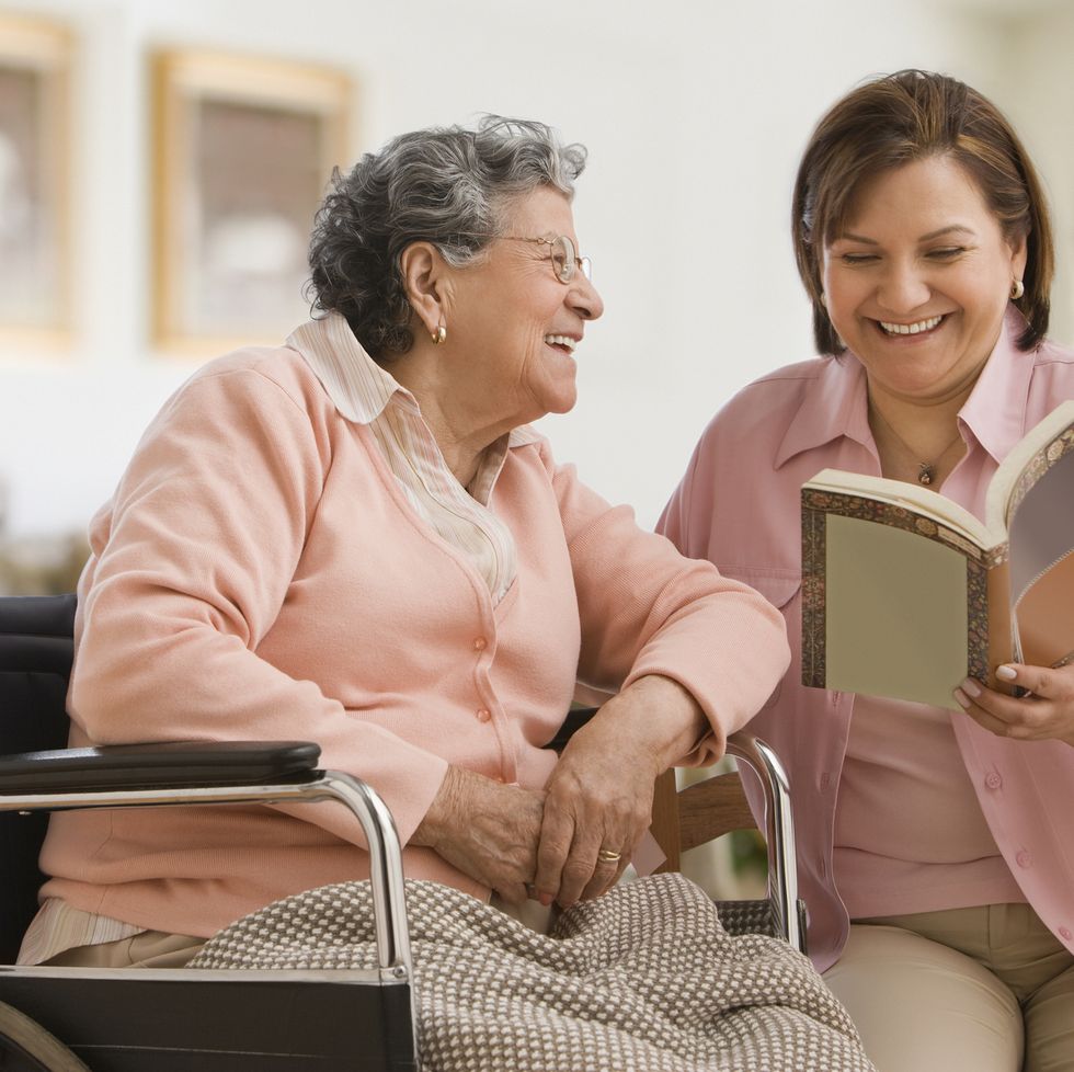 hispanic woman reading to another woman in a wheelchair