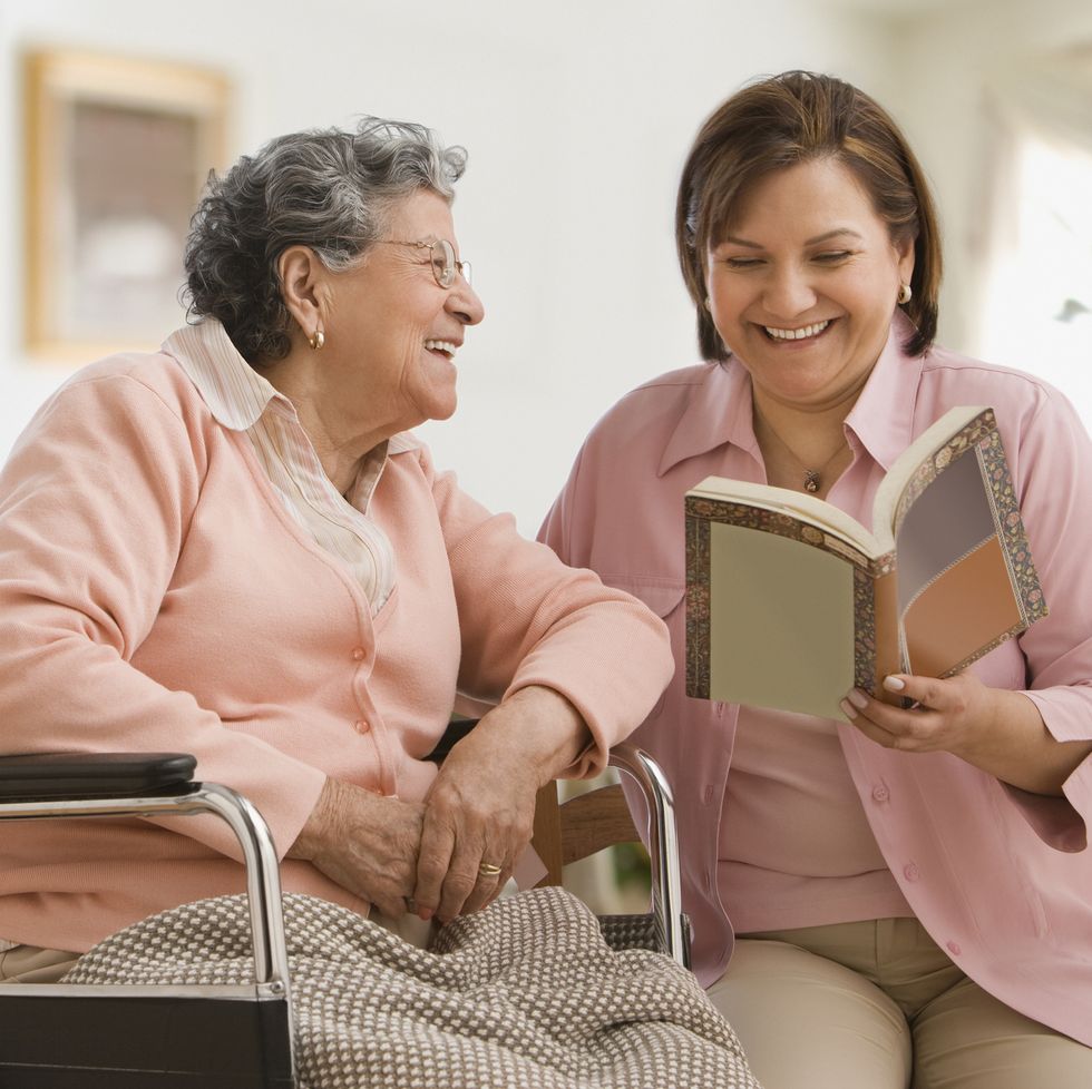hispanic woman reading to another woman in a wheelchair