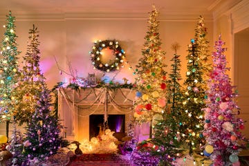 living room with many colorful, flocked, lighted christmas trees, a wreath over the fireplace, mantel decorations, and little globes inside the fireplace itself