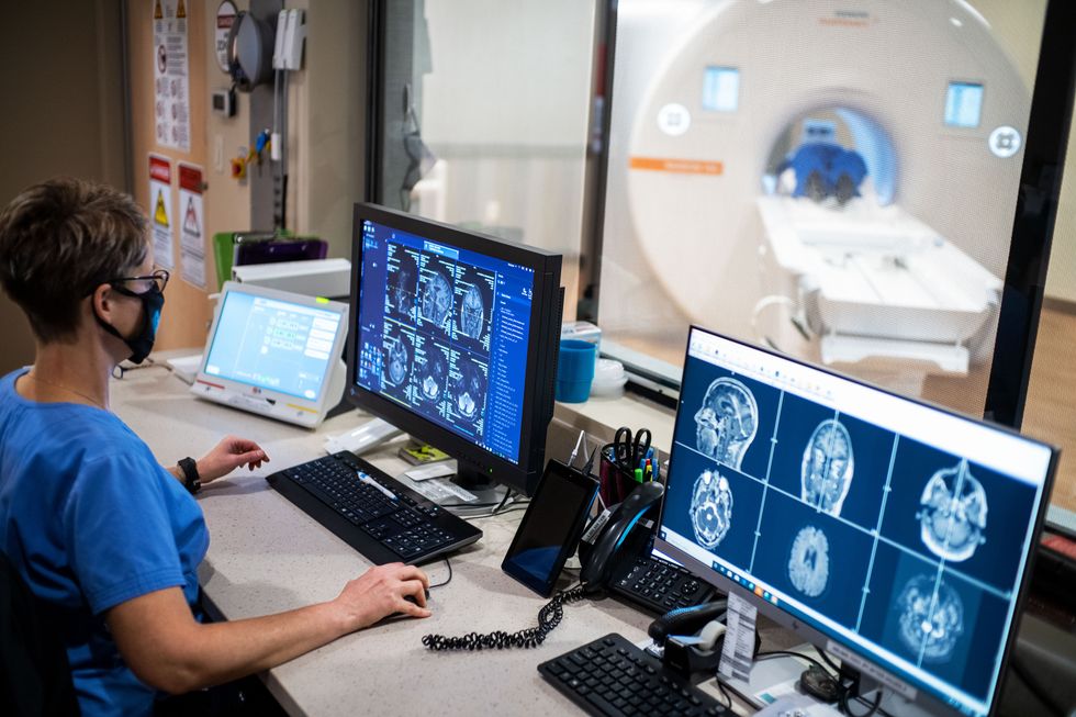 doctor looking at two screens of brain scans while patient is in an x ray tube