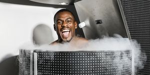 this is a man standing, smiling excitedly, in a cryotherapy unit, with cold air blowing out of it the unit itself is black and silver