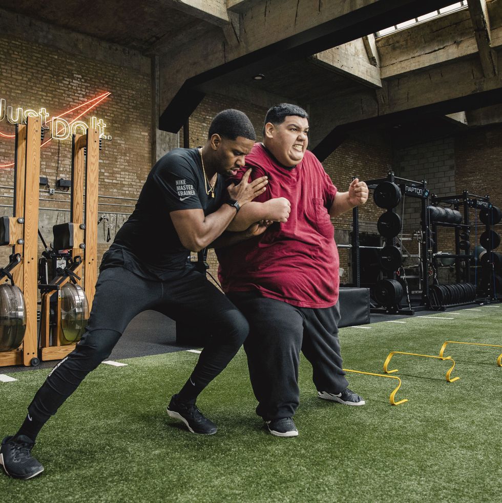 large man in gym working out with trainer on astroturf