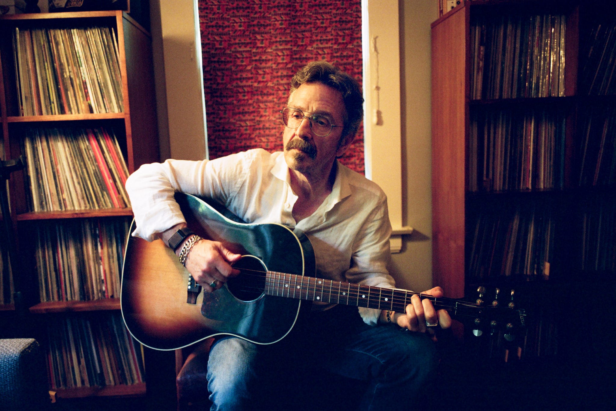 marc maron playing guitar in a room filled with vinyl records