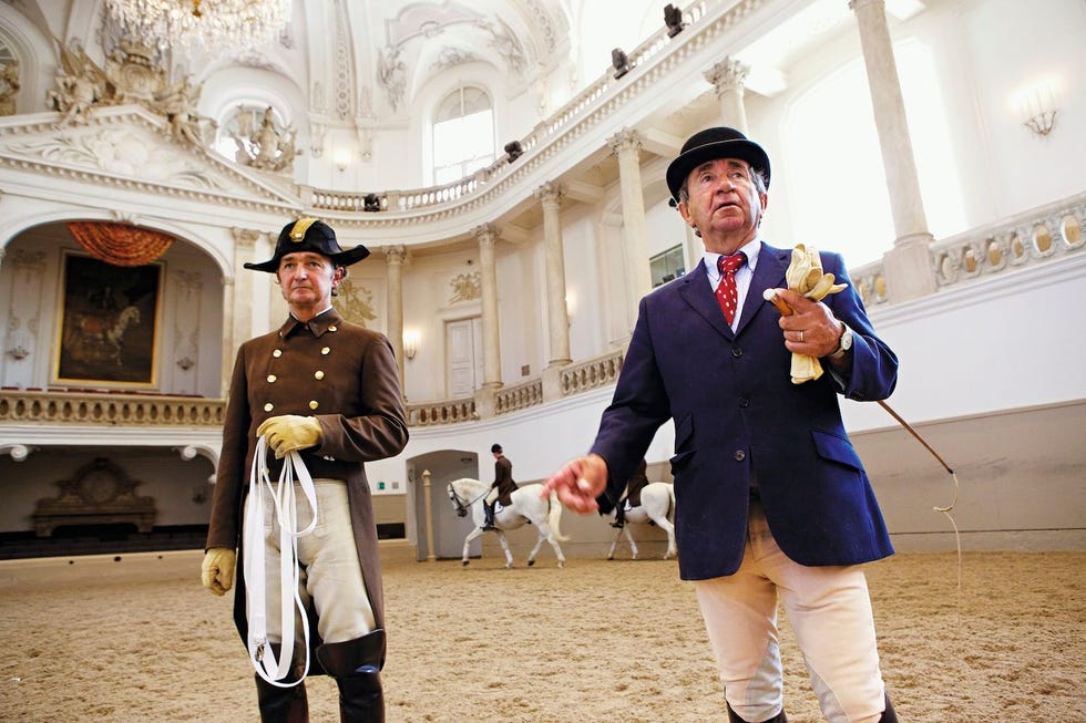 Lipizzaner hengsten oefenen in de Spaanse Rijschool in Wenen de oudste klassieke dressuuropleiding ter wereld terwijl directuer Ernst Bachinger toeziet van onder zijn bolhoed