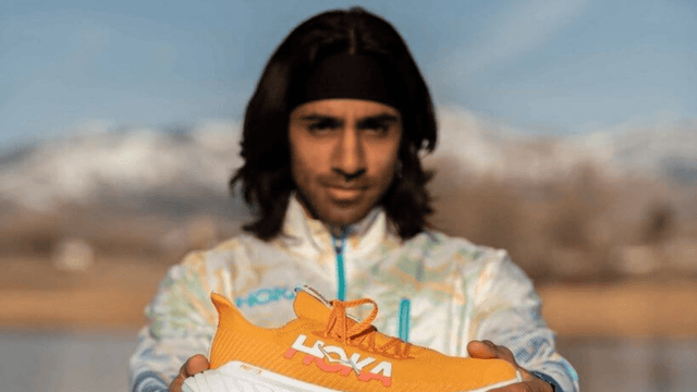 a person holding a pair of orange athletic shoes against a scenic background