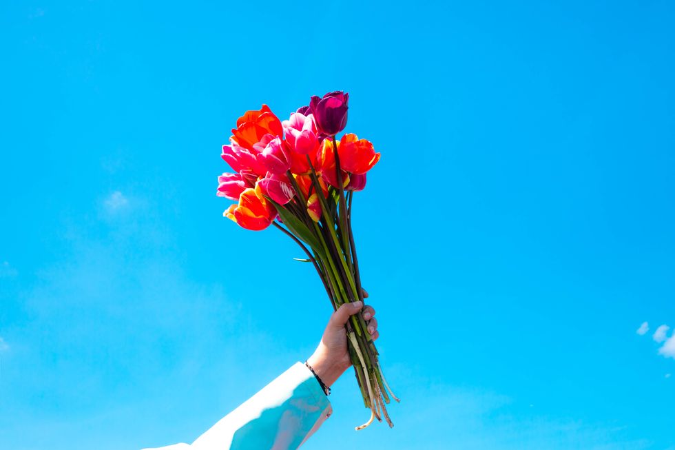 holding a bouquet of tulips in the air against the blue sky in the netherlands