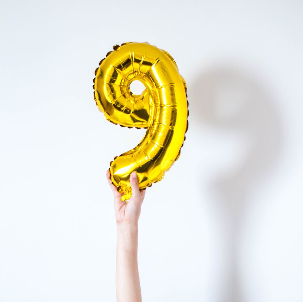 holding a golden colored inflatable balloon number nine