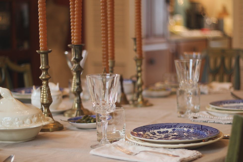 holiday table set with thrifted and collected vintage dishes, silverware and candlesticks. antique blue and white china with thrifted sterling silverware. a variety of brass candlesticks decorating the dining room table. celebration and holiday meal.