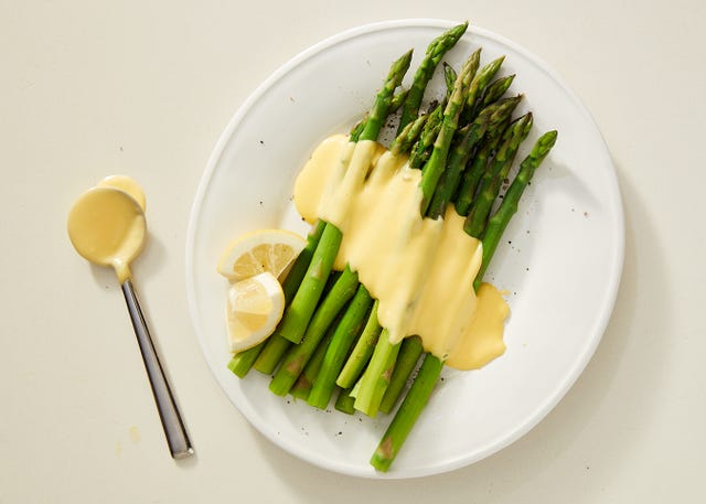 asparagus topped with hollandaise on a white plate garnished with lemon wedges