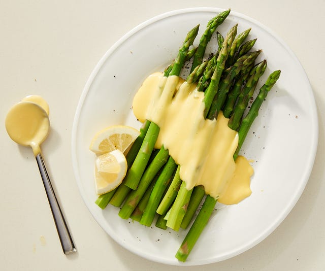 asparagus topped with hollandaise on a white plate garnished with lemon wedges asparagus topped with hollandaise on a white plate garnished with lemon wedges