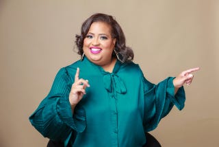 a woman in a teal blouse gestures with her hands