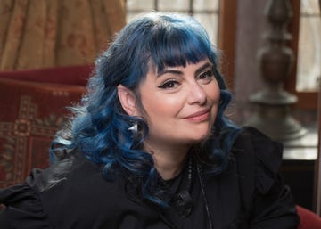 person with blue hair and black clothing seated in a room