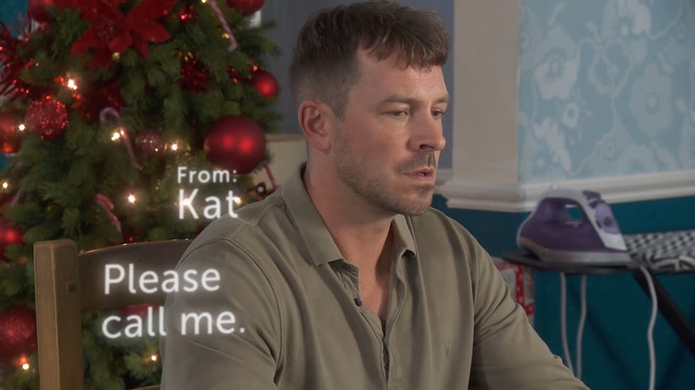 hollyoaks, darren gets a text from kat, he looks concerned, there's a christmas tree behind him