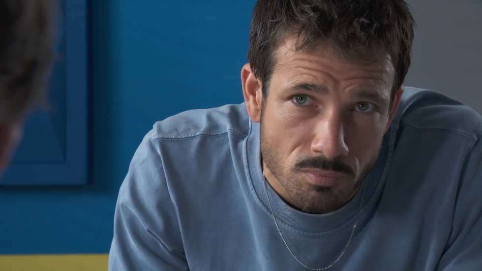 hollyoaks, dodger in a blue tshirt in the police interview room, leaning forward with a serious look on his face