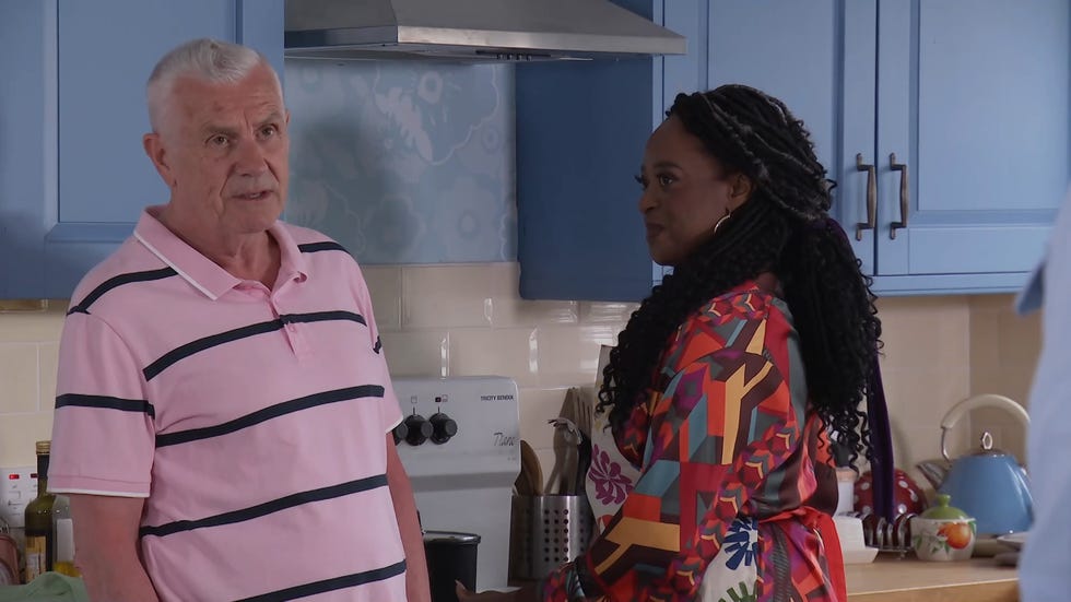 hollyoaks, jack osborne in a pink t shirt in the kitchen next to pearl, wearing a multicoloured outfit with an apron