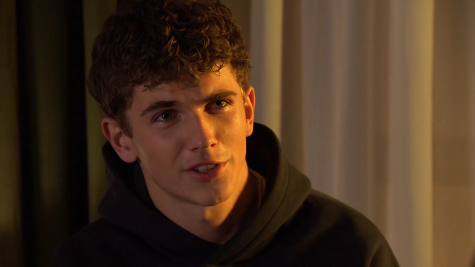 hollyoaks, lucas hay in a black hoodie, lit in an orange glow