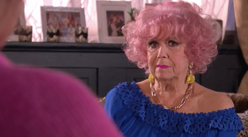 hollyoaks, diane langton as nana mcqueen with pink hair, big earrings and a blue outfit