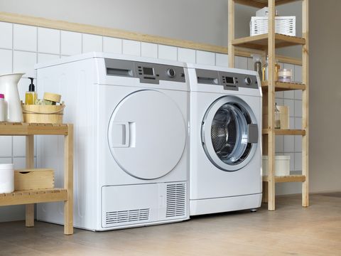 เครื่องซักผ้าและเครื่องอบผ้าสีขาวสไตล์โมเดิร์นวางเคียงข้างกันระหว่างชั้นวางไม้ 2 ชั้น อันหนึ่งยาวและอีกอันสั้น
