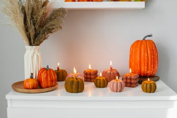 calabazas naranjas decoradas con velas encendidas sobre pared blanca