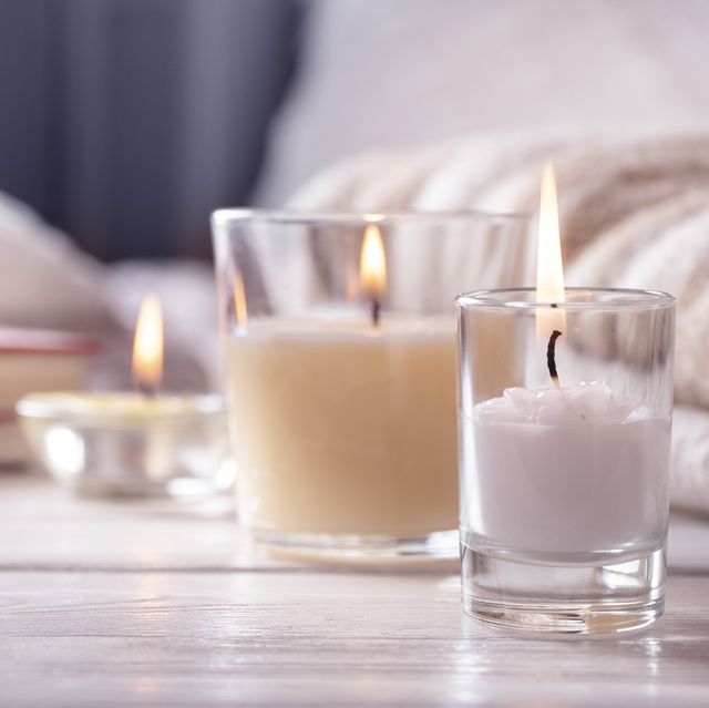 home interior still life with detailes several candles on white wooden table in front of bed, the concept of cosiness