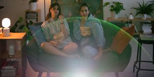 two women on couch in living room eating popcorn and watching a movie from a projector screen