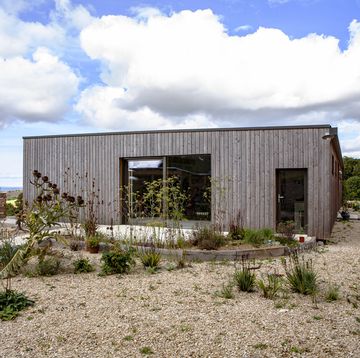 a new build wood clad single story house with gravel garden and views over hills beyond