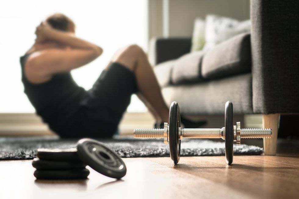 Home workout. Man doing ab training and crunches in living room gym. Guy doing sit ups. Warm up before weight exercise. Fitness concept with dumbbell.