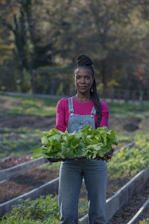 woman in overalls holding lettuce in a field