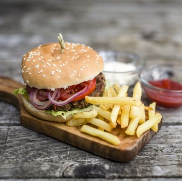 Homemade burger with lettuce, meat, tomato, onion and french fries on chopping board