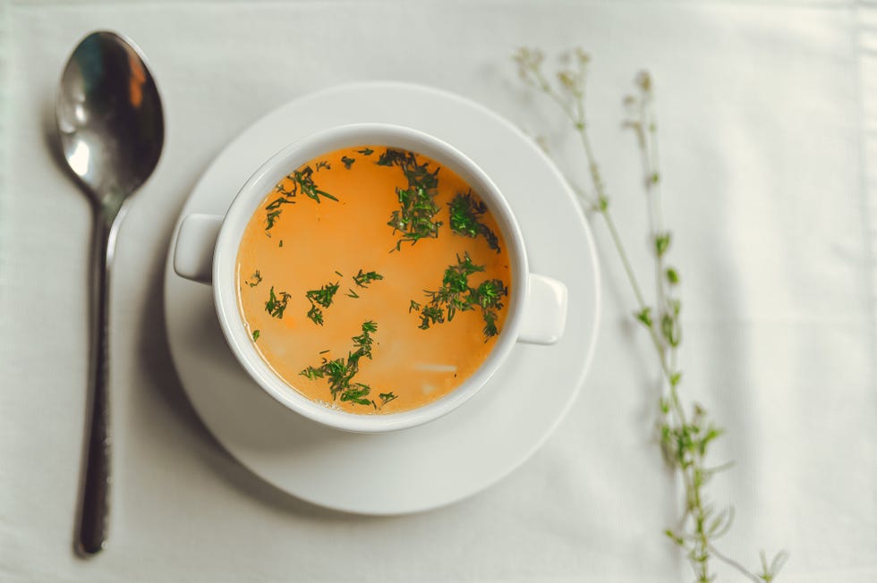 chicken soup with noodles and herbs in a beautiful white plate on a white table, white background top view