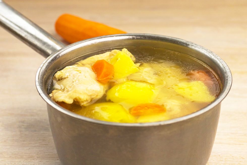homemade chicken soup with vegetables in metal ladle pot on wooden table background